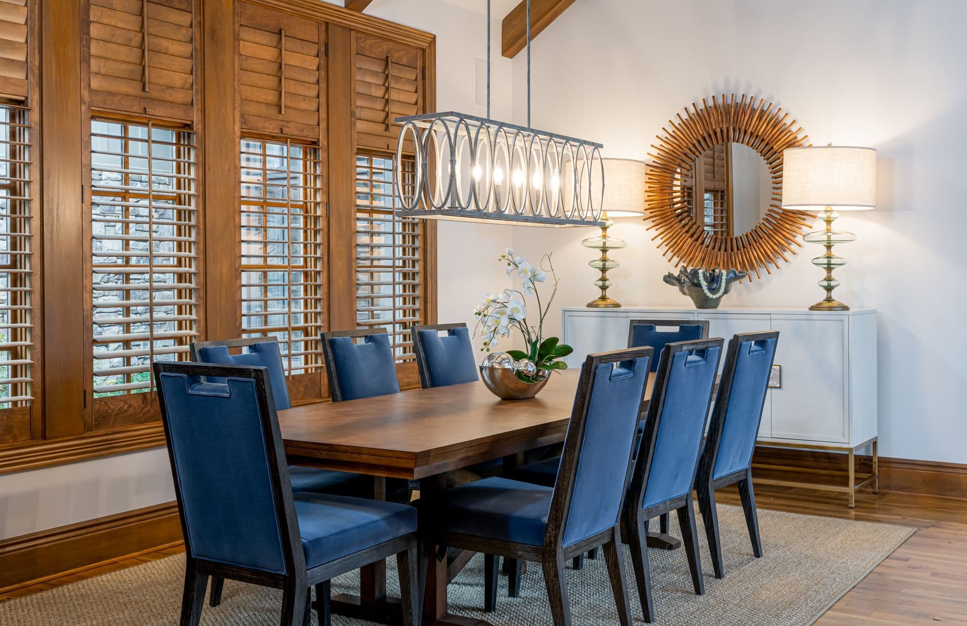 A welcoming living room with warm wood shutters and a sunburst mirror